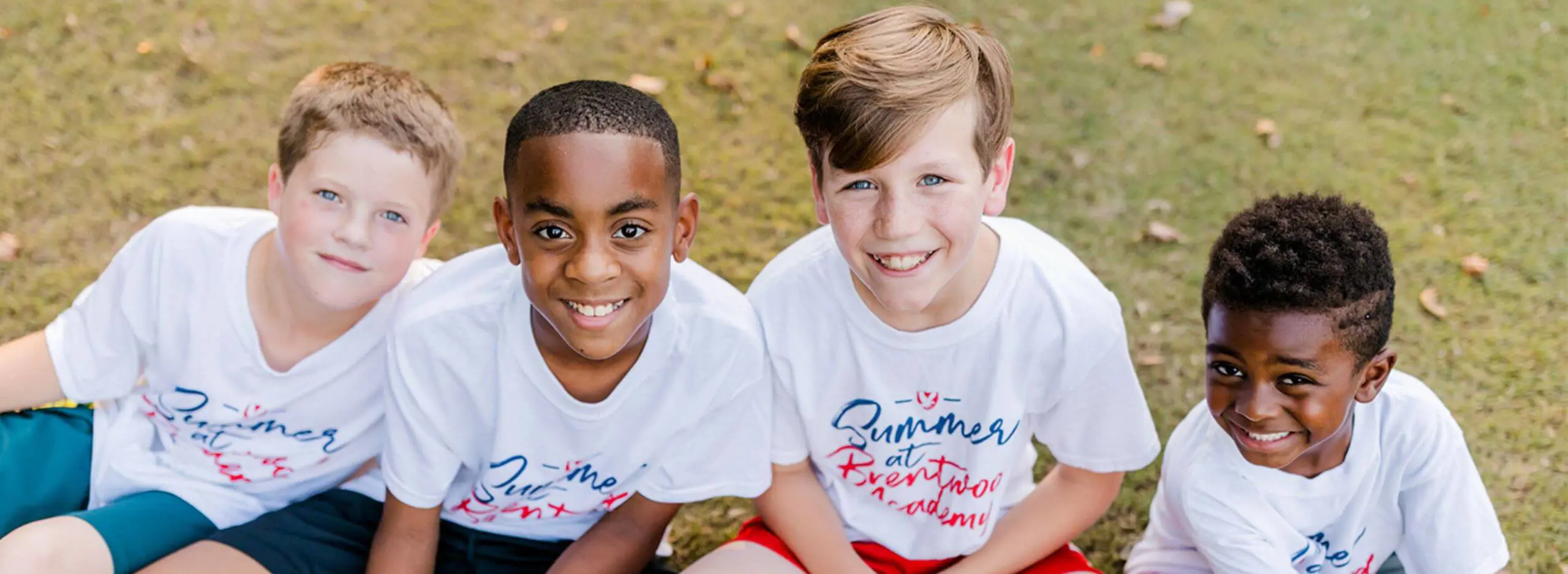 Children attending BA Summer camp sitting on the grass and smiling